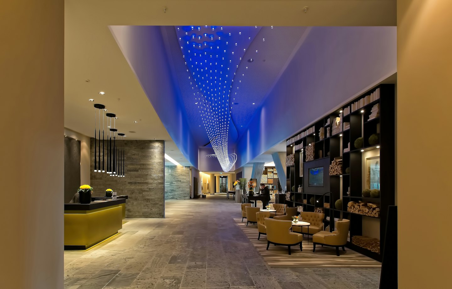 Modern hotel lobby with a golden reception desk and blue-lit ceiling.